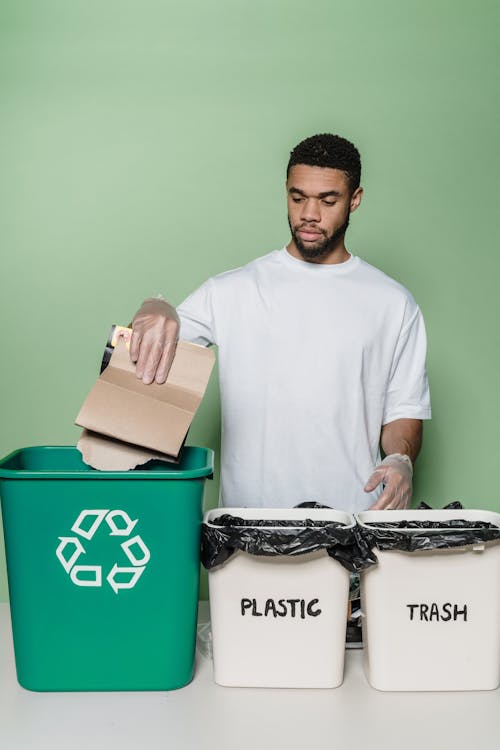 A Man Segregating Trash while Holding a Cardboard
