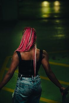 Stylish woman with pink braids in a tank top stands indoors, showcasing vibrant fashion.