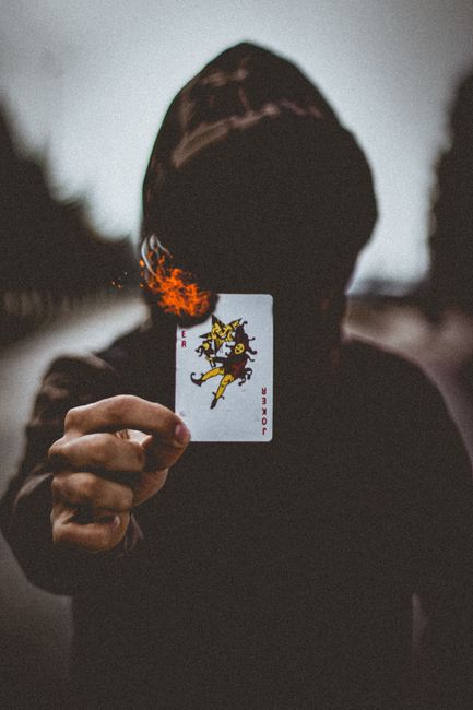 A person holding a burning Joker card in a hooded cloak, creating a moody atmosphere.