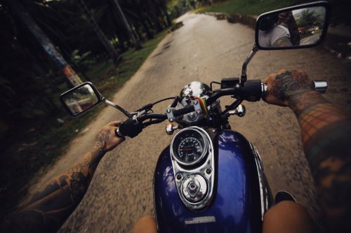 Free POV shot of riding a motorcycle on a scenic road with tattooed arms visible. Stock Photo