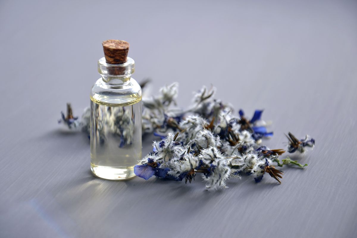 Close-up of a glass bottle of lavender oil surrounded by dried lavender flowers, illustrative photo