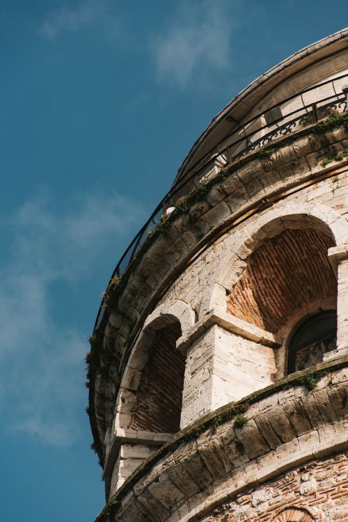 Free Low angle view of an ancient stone tower with arched windows and intricate architecture against a blue sky. Stock Photo