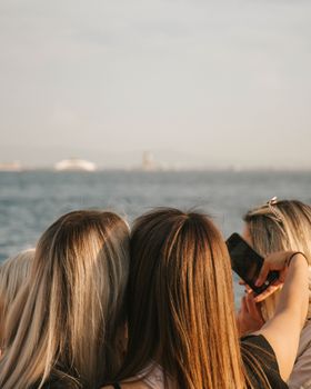 Three women capture a moment by the ocean using a smartphone.
