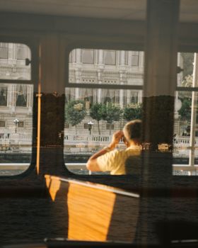 Urban man looking through boat window with city reflection, captured at sunset.