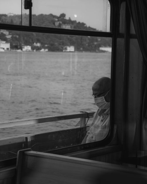 Free A man wearing a face mask sits quietly on a boat, gazing at the sea, visible through a window. Stock Photo