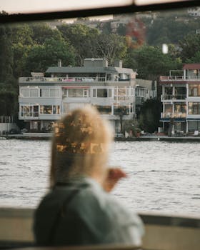 A person views modern waterfront buildings through reflective glass, creating a serene urban scene.