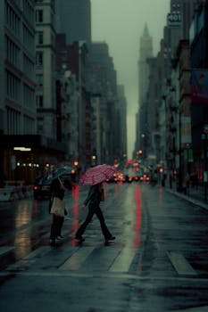 Two people crossing a rainy New York street with umbrellas and reflections.
