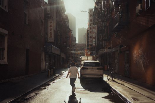 A person walking down a twilight street in Chinatown, New York City, with vibrant signs and urban architecture.