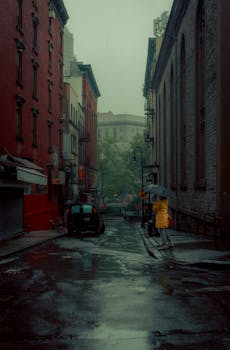 A person in a yellow raincoat walks down a rainy street in New York City, holding an umbrella.