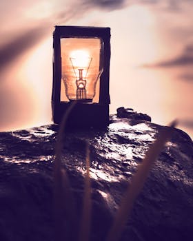 A vintage lightbulb on a rock at sunset, emitting a warm glow, evoking a sense of tranquility and nostalgia.