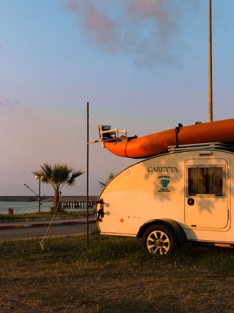 Vintage Camper With An Orange Dinghy On Roof At Sunset