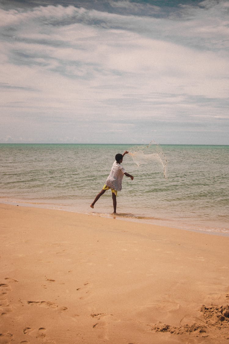 Boy Standing On Seashore Casting A Fishing Net 