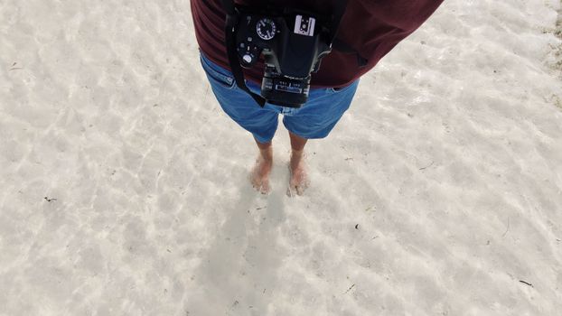 Photographer with DSLR standing barefoot on sandy beach in the Maldives.