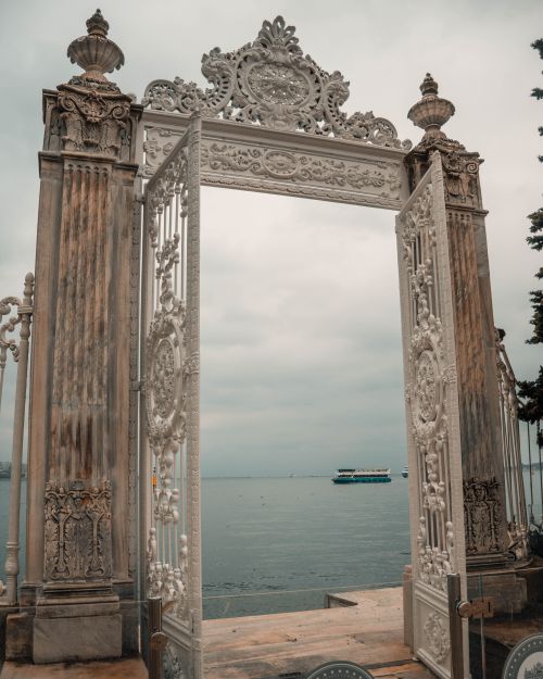 Free Elegant historic gate opens to a scenic sea view, under a cloudy sky. Stock Photo
