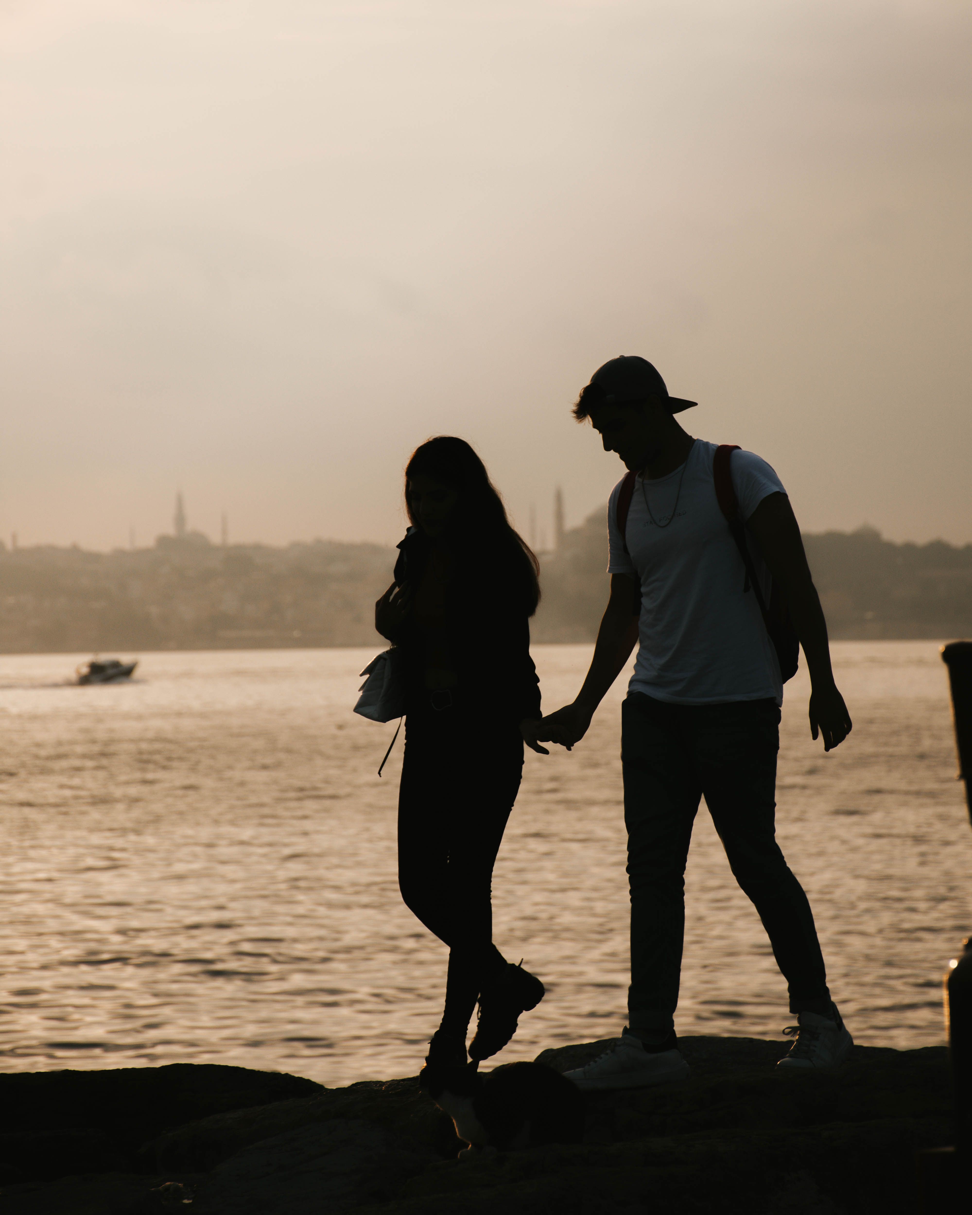 Silhouette of a couple holding hands by the sea at sunset, evoking romance and tranquility.