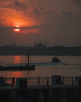 Dramatic sunrise over Bosporus Strait, Istanbul, showing the city skyline and a boat in silhouette.