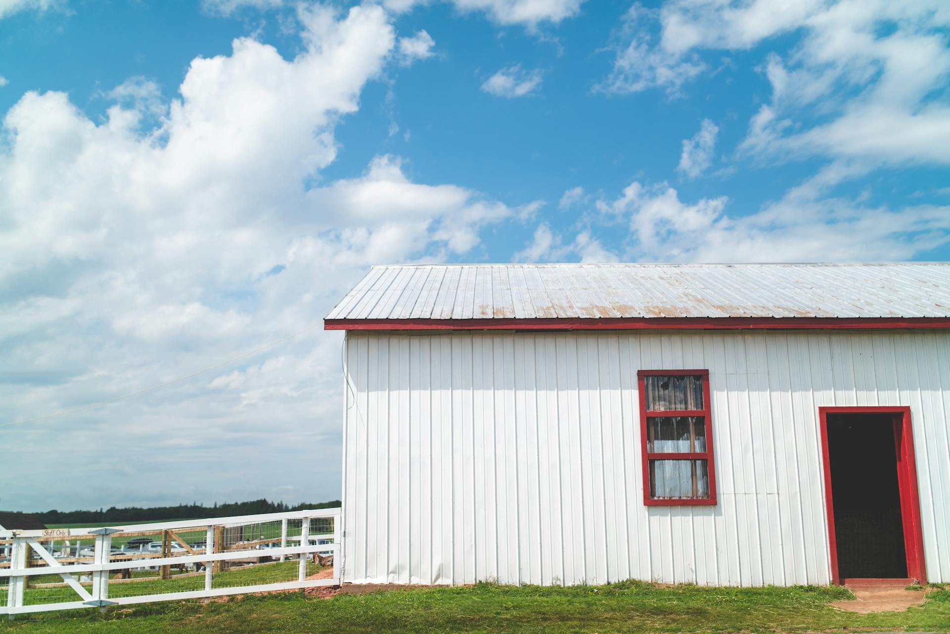 Capture of a white barn with red trim against a blue sky with clouds. Ideal rural setting.