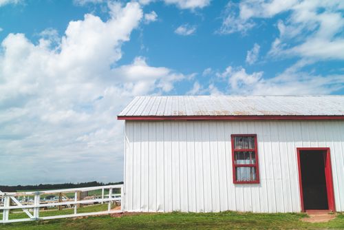Free Capture of a white barn with red trim against a blue sky with clouds. Ideal rural setting. Stock Photo