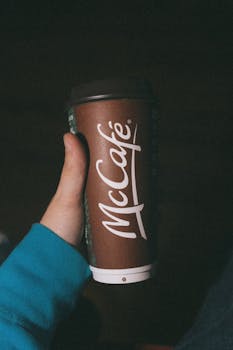 A person holds a McCafé coffee cup featuring brown sleeve and logo.