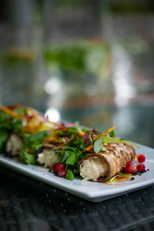 Free Delicious eggplant rollatini garnished with fresh greens and pomegranate seeds on a white plate. Stock Photo