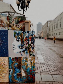 A vibrant display of paintings on a city street, showcasing urban art in a rainy, moody setting.