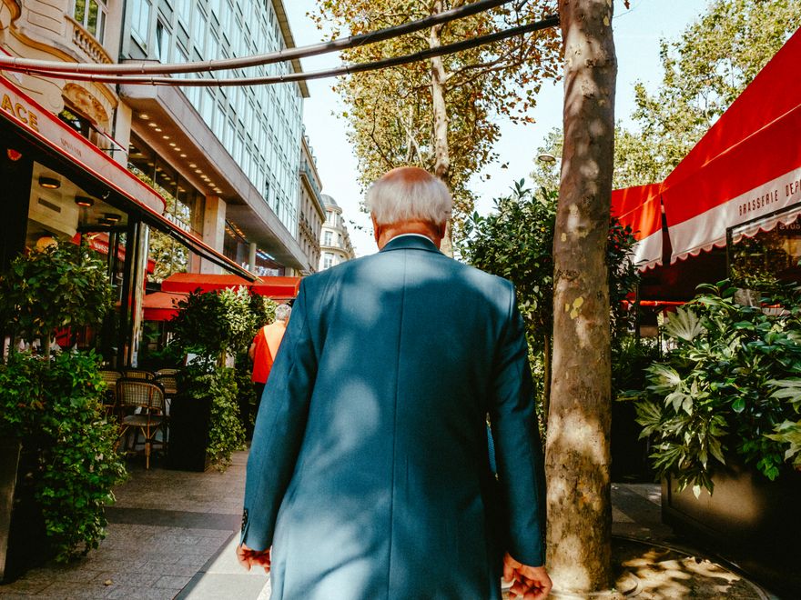 A man in a suit walking past pavement cafés in warm afternoon light — photo by Mathias Reding on Pexels