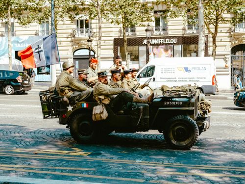 Free Soldiers in vintage military uniforms riding a jeep during a city parade. Stock Photo