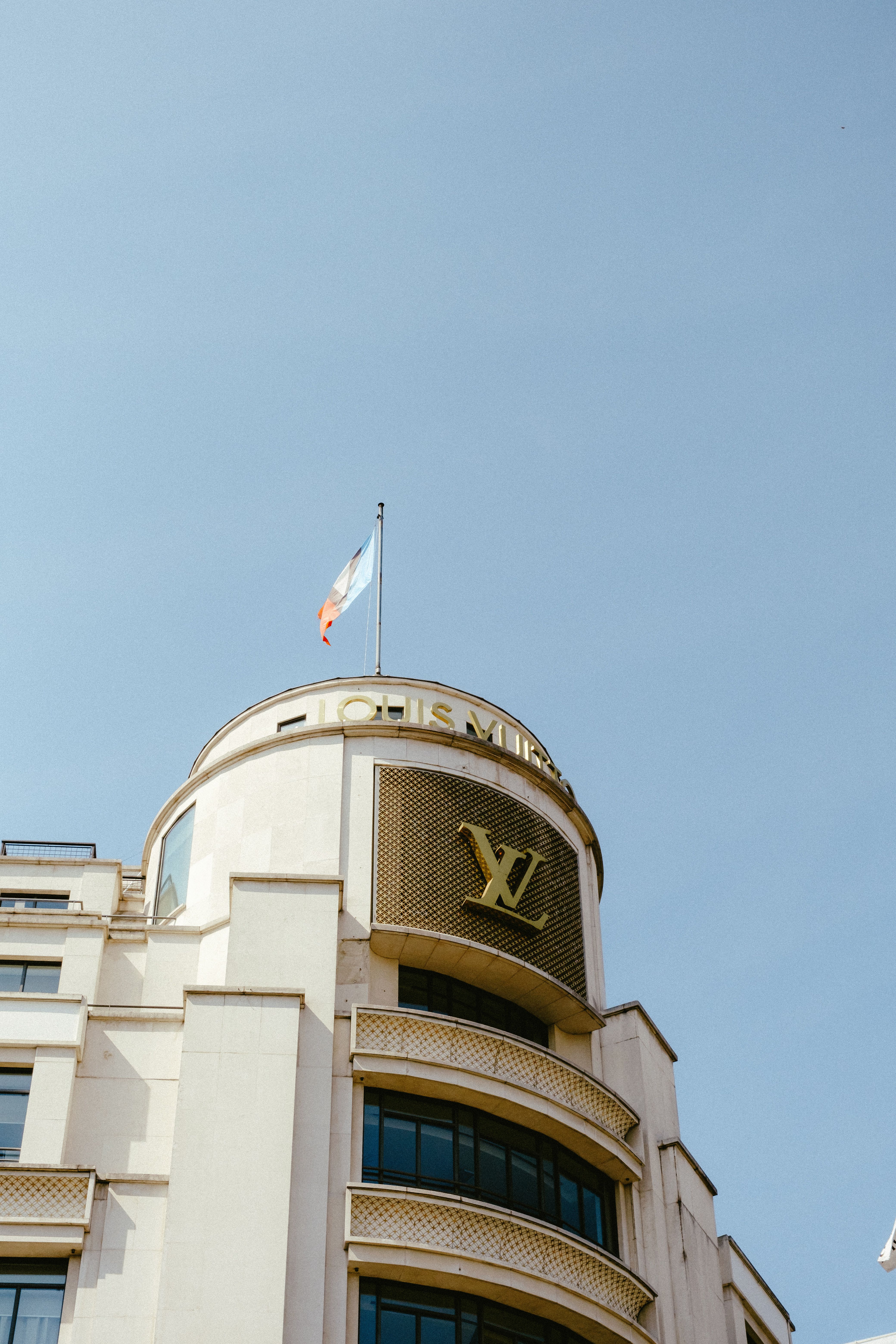 Low angle shot of a high-rise building with glass windows and flag waving.