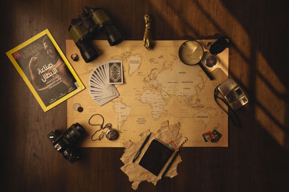 A styled flat lay of travel essentials including a map, camera, and binoculars.