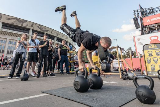 Man performing handstand on kettlebells during outdoor fitness event.