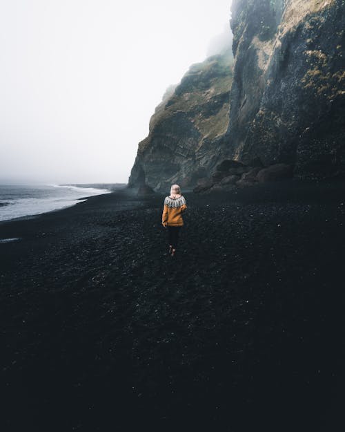 Back View of a Woman Walking on Black Sand