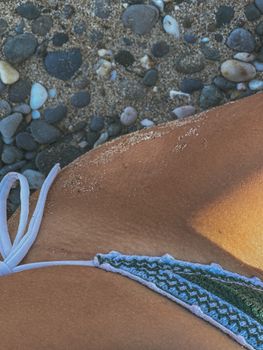 Close-up of a person's hip on a pebbly beach with swimwear and sand.