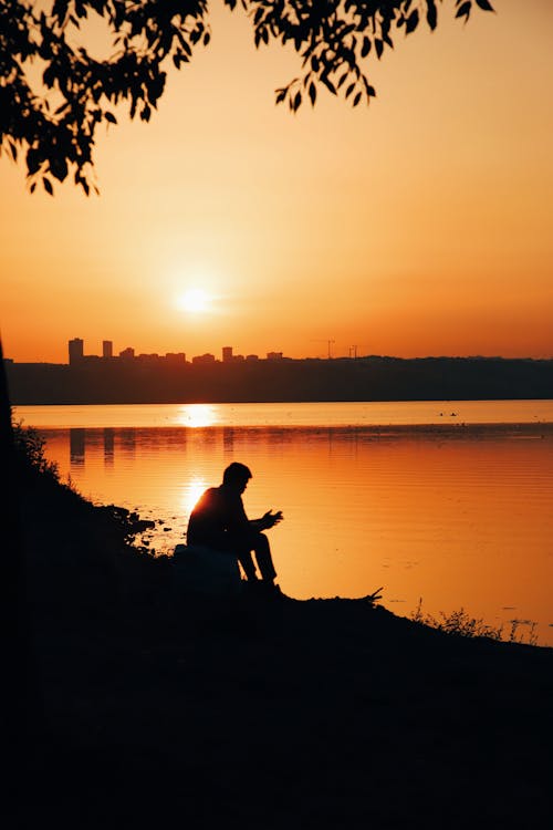 A Silhouette of a Man Sitting Near the Sea