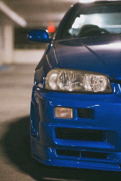 Free Detailed view of a blue car's front bumper and headlight indoors, emphasizing automotive design. Stock Photo