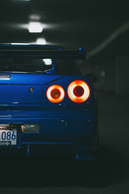 Free Rear view of a blue sports car with glowing tail lights in a dimly lit parking garage. Stock Photo