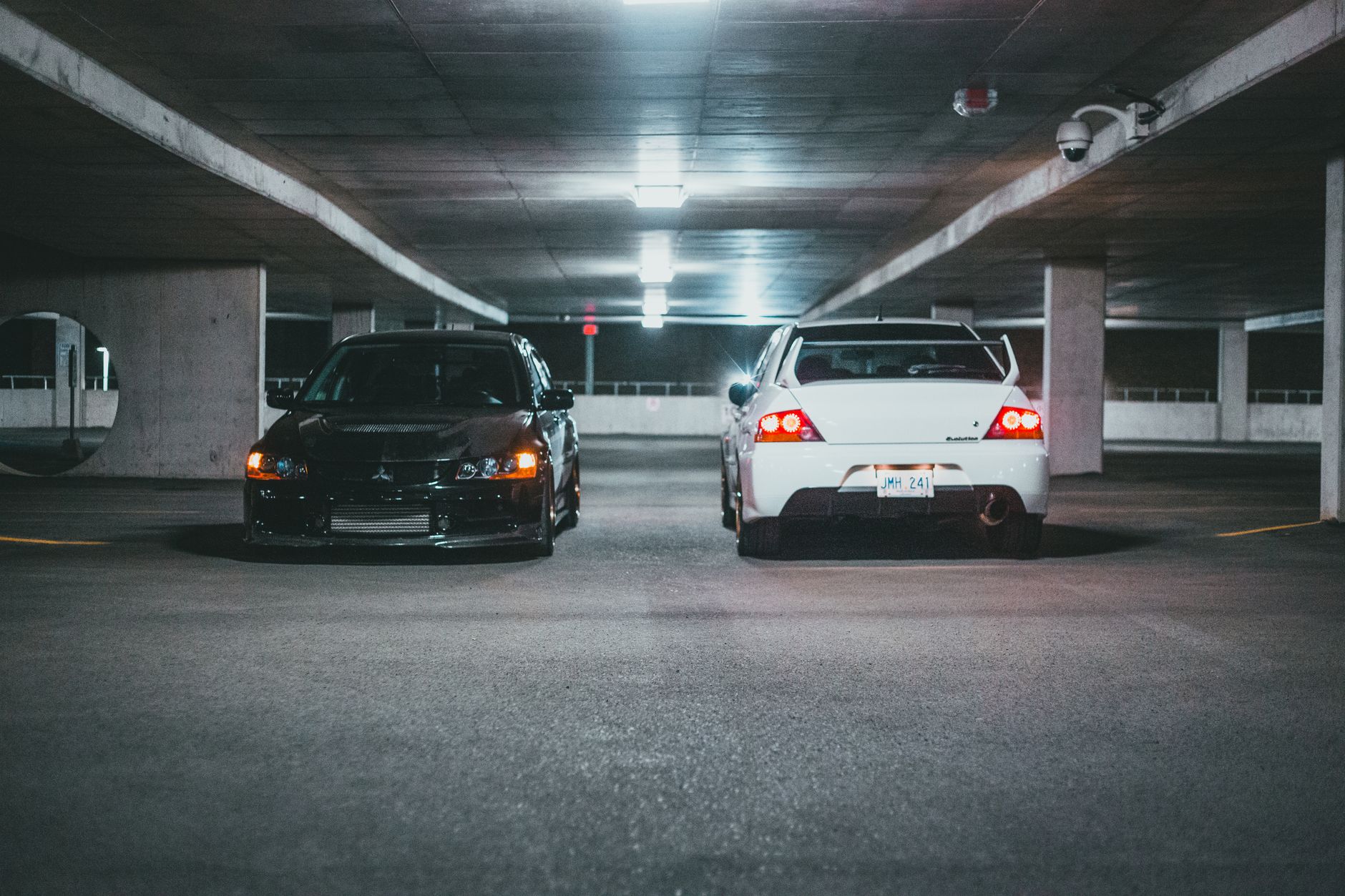 Black and white sedans parked in a dimly lit urban underground parking garage at night.