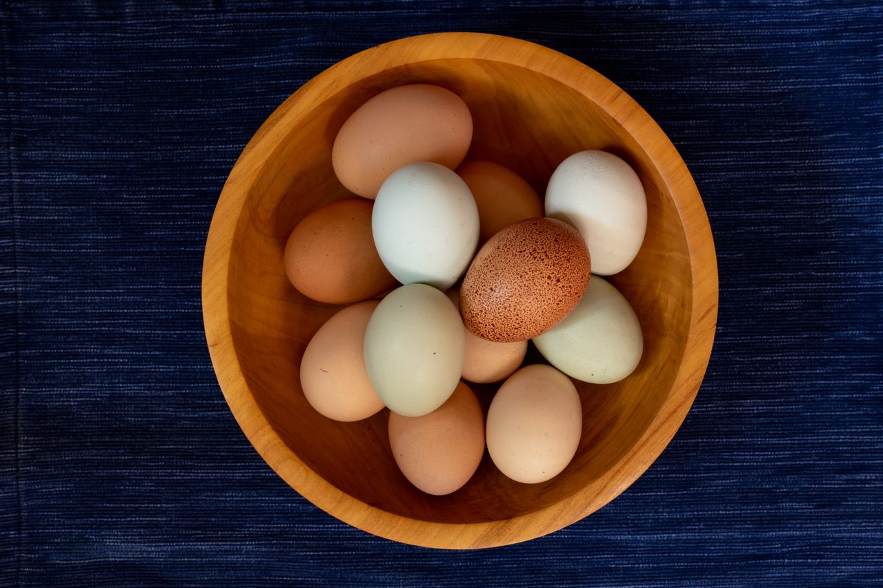 a variety of colorful chicken eggs arranged in a wooden bowl on a dark
