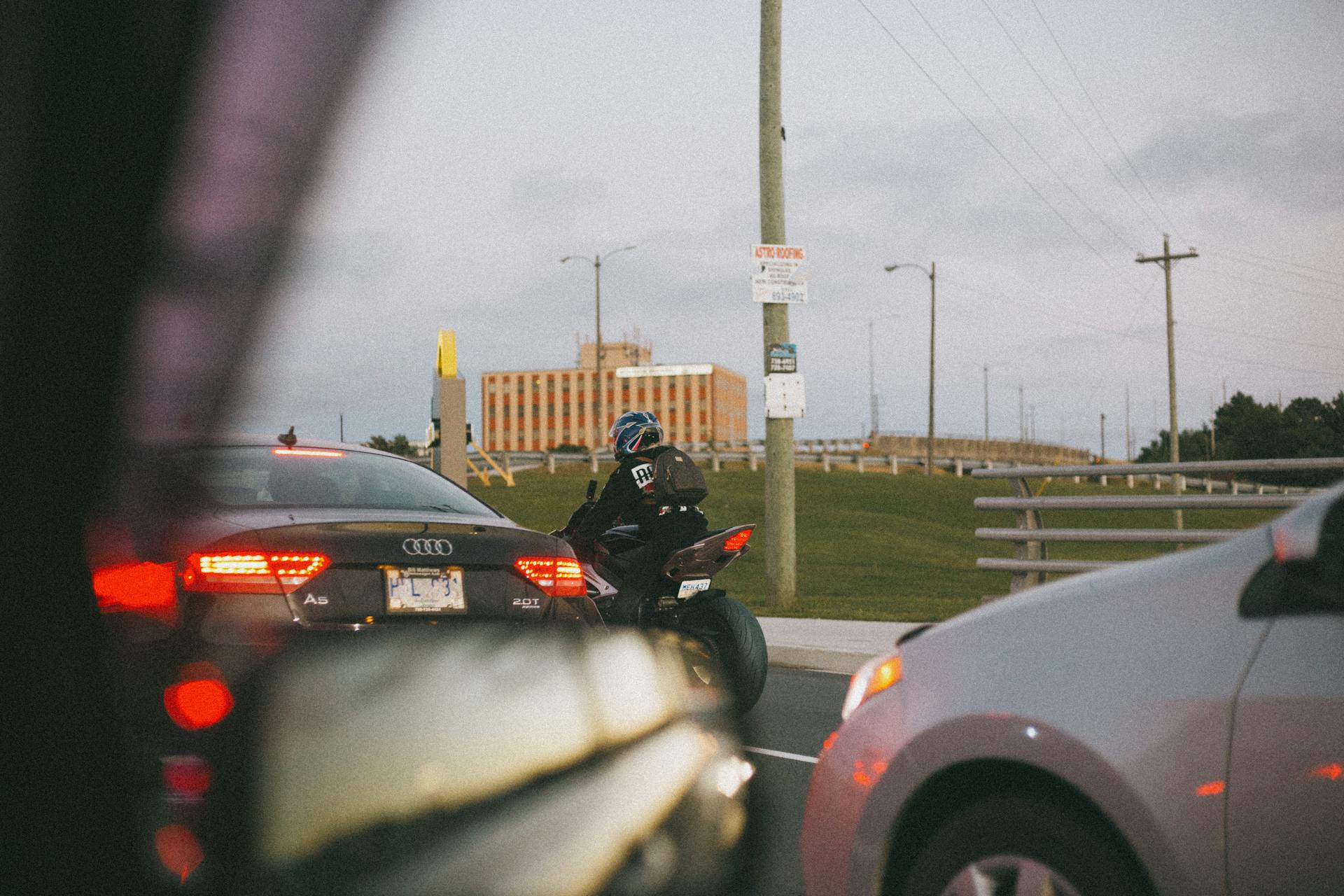 A busy urban road with cars and a motorcycle waiting at a traffic light.