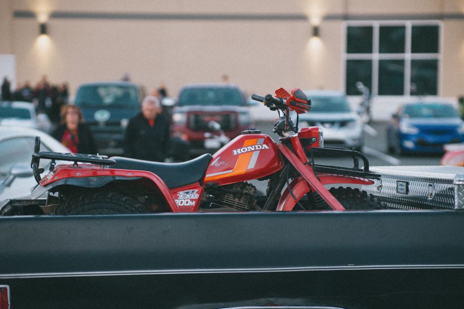 A red quadbike secured on a truck in a crowded parking lot.