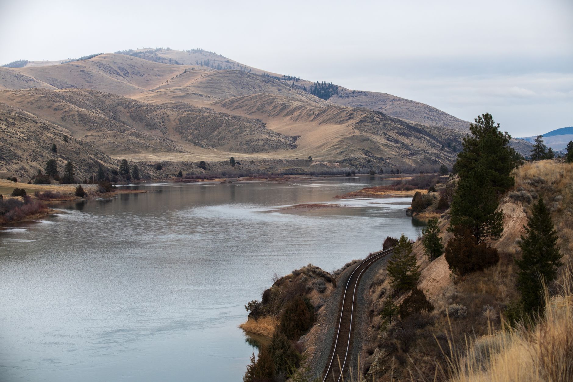 Peaceful river with mountains and railway in Montana's natural landscape.