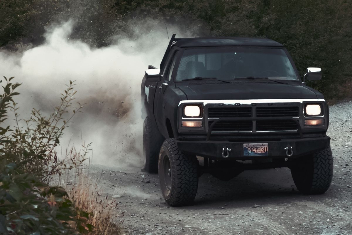 Pickup truck driving fast on a loose gravel road kicking up a dust cloud on a rural washboard road