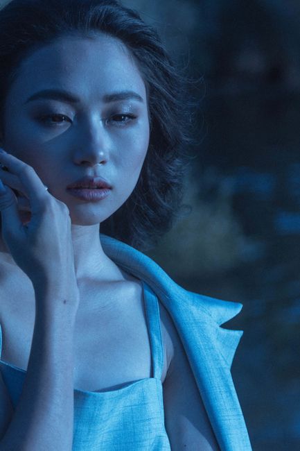 A sophisticated pose of an Asian woman with a serious expression captured in an artistic blue light.
