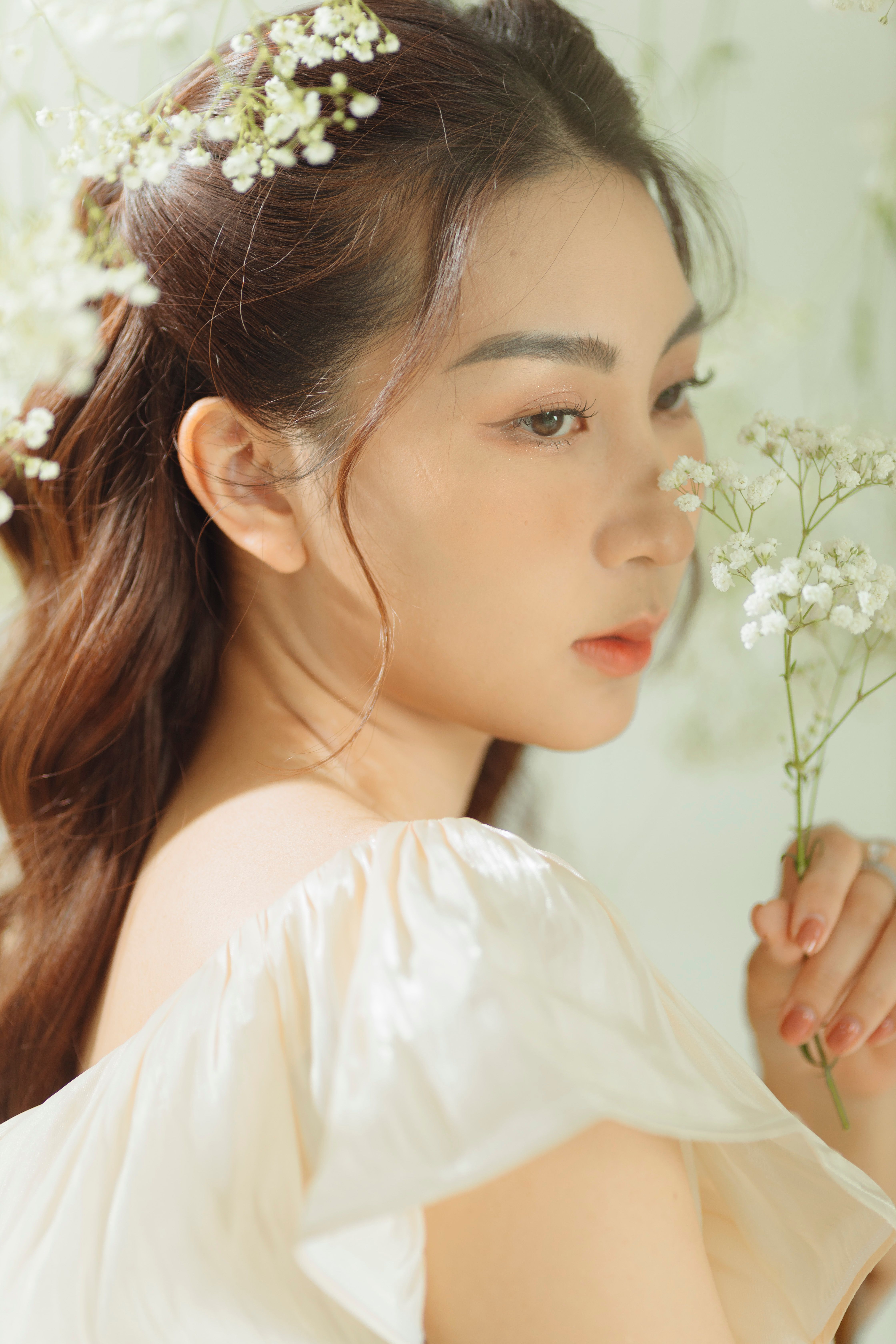Elegant portrait of an Asian woman surrounded by delicate white flowers, exuding beauty and grace.