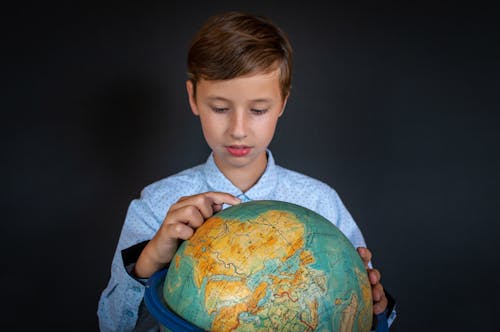 Boy in Blue Long Sleeve Shirt Studying the Globe