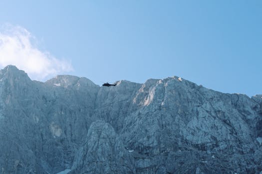 A helicopter soaring against the backdrop of majestic rocky mountains under a clear blue sky.