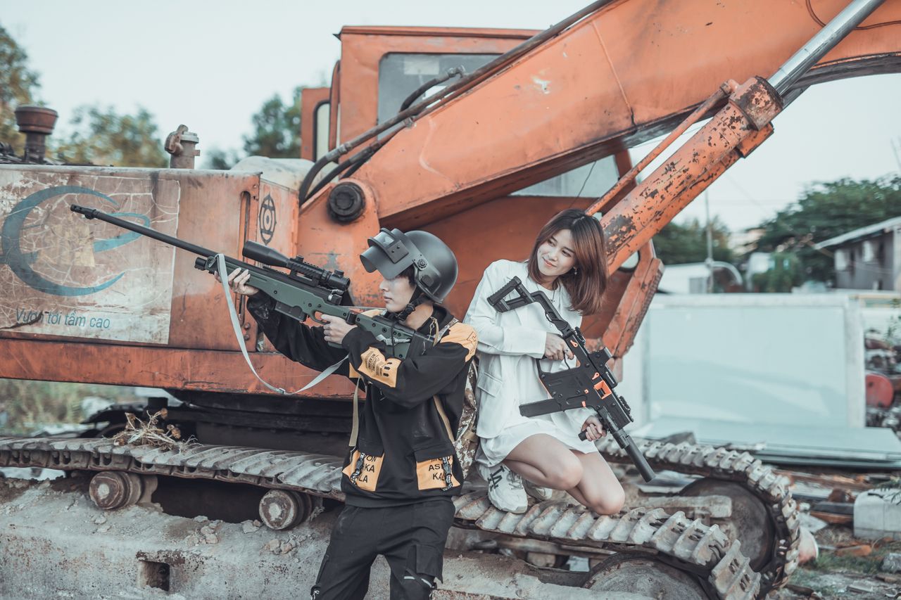 a playful young couple posing with toy guns atop an old excavator on a