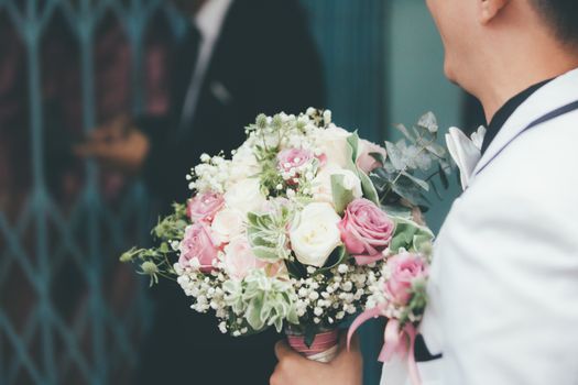 A groom holds a beautiful floral bouquet with roses and baby's breath, ideal for weddings.