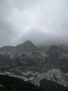 Dramatic mist-covered rocky mountains under a gloomy and cloudy sky, creating a mysterious landscape.