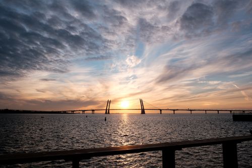Free Capture of a serene sunset over a long suspension bridge with dramatic clouds and calm sea. Stock Photo
