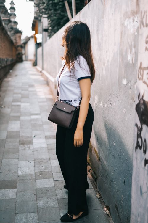 Free A stylish young woman poses in an urban alley, showcasing her outfit and accessories. Stock Photo